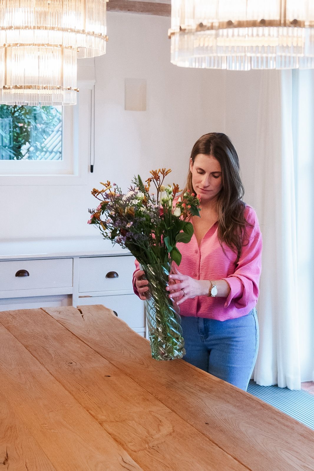 Vrouw met roze blouse die groene vaas met bloemen vasthoudt 